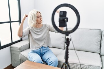 Sticker - Young caucasian woman recording vlog tutorial with smartphone at home showing arms muscles smiling proud. fitness concept.