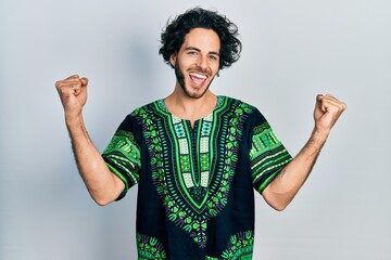 Sticker - Handsome hispanic man wearing traditional african clothes screaming proud, celebrating victory and success very excited with raised arms