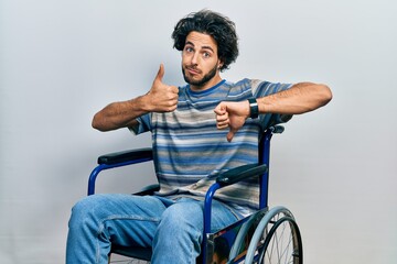 Wall Mural - Handsome hispanic man sitting on wheelchair doing thumbs up and down, disagreement and agreement expression. crazy conflict