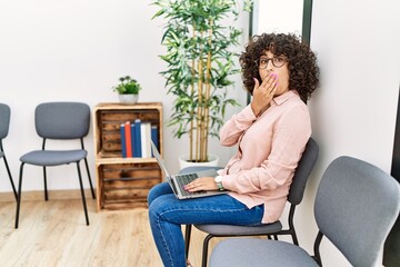 Sticker - Young middle eastern woman sitting at waiting room working with laptop covering mouth with hand, shocked and afraid for mistake. surprised expression