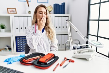 Poster - Young beautiful doctor woman with reflex hammer and medical instruments bored yawning tired covering mouth with hand. restless and sleepiness.