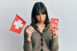 © Krakenimages.com - Young hispanic woman holding swiss flag and passport depressed and worry for distress, crying angry and afraid. sad expression.