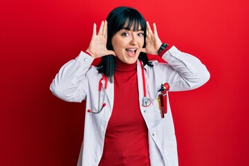 Poster - Young hispanic woman wearing doctor uniform and stethoscope smiling cheerful playing peek a boo with hands showing face. surprised and exited