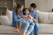 © fizkes - Caring bonding happy millennial couple parents holding on laps sincere cute small child daughter, enjoying carefree playtime together at home, resting on comfortable couch in modern living room.