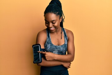 Wall Mural - African american woman with braided hair wearing sportswear using arm band smiling and laughing hard out loud because funny crazy joke.