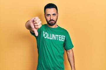 Canvas Print - Handsome hispanic man with beard wearing volunteer t shirt with angry face, negative sign showing dislike with thumbs down, rejection concept