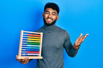 Arab man with beard holding traditional abacus celebrating achievement with happy smile and winner expression with raised hand