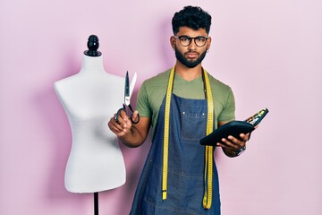 Canvas Print - Arab man with beard dressmaker designer holding scissors and sewing kit skeptic and nervous, frowning upset because of problem. negative person.