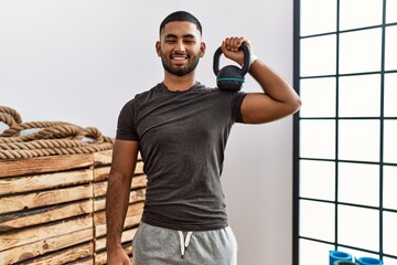 Canvas Print - Young indian man wearing sportswear using dumbbells looking positive and happy standing and smiling with a confident smile showing teeth