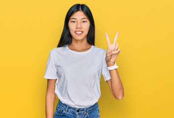 Beautiful young asian woman wearing casual white t shirt showing and pointing up with fingers number two while smiling confident and happy.