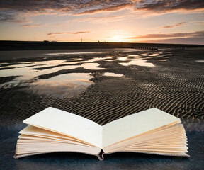 Wall Mural - vibrant sunrise landscape reflected in low tide water on beach coming out of pages in book composite