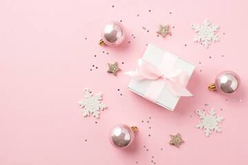 Wall Mural - Top view photo of pink christmas decorations balls glowing stars sequins snowflakes and white gift box with pink ribbon bow on isolated pastel pink background with copyspace