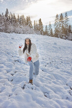 Winter Woman Playing In Snow Throwing Snowball At Camera Smiling Happy Having Fun Outside On Snowing Winter Day In Front Of Mountain Forest. Beautiful Joyful Multicultural Asian Caucasian Girl