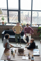 Poster - Group of young co-workers in casualwear discussing ideas for new business project at meeting in large office