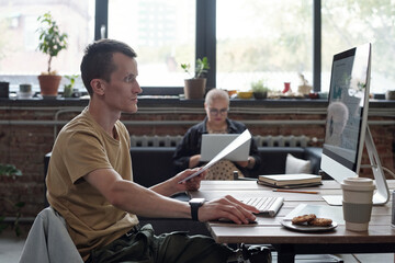Poster - SIde view of serious young businessman looking at computer screen while analyzing financial data against female colleague