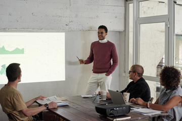 Poster - Young successful business coach standing by interactive whiteboard while explaining financial data to group of colleagues
