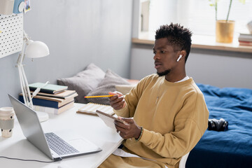 Poster - Young African man with pencil pointing at laptop screen while communicating with teacher during online lesson