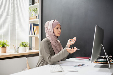Aufkleber - Young Muslim female teacher with pen explaining something to online audience while sitting in front of computer monitor