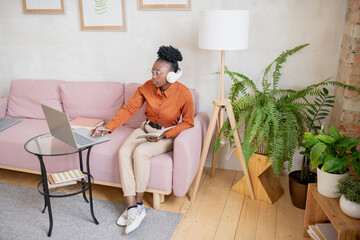 Aufkleber - Contemporary young serious black woman with copybook sitting on sofa in front of laptop during online lesson