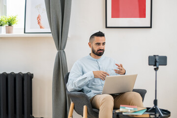 Poster - Young bearded teacher or coach sitting in front of smartphone camera and interacting with online audience