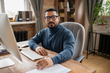 Aufkleber - Serious middle aged teacher looking at camera while sitting by desk in front of computer monitor in home environment