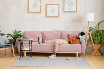 Poster - Young relaxed African woman with tablet lying on couch and watching online video in home environment