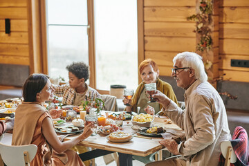 Happy young woman and mature man with drinks interacting by festive table against little boy and aged female