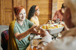 © pressmaster - Smiling mature female taking homemade food held by her husband while helping to serve festive table for family dinner