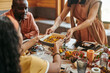 © pressmaster - Interracial girl helping her mother while taking bowl with homemade food over served festive table during family dinner