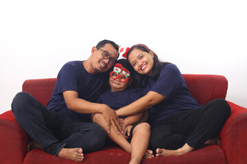 Wall Mural - Asian family celebrating Christmas and New Year while sitting on red sofa. Isolated on white background