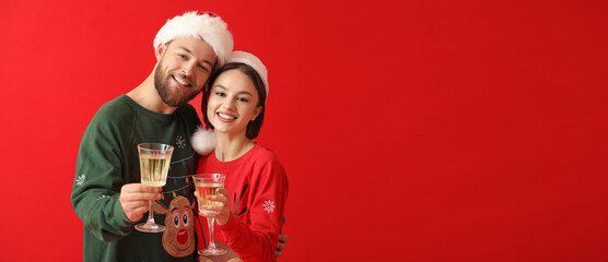 Wall Mural - Young couple in stylish Christmas clothes and with glasses of champagne on color background with space for text