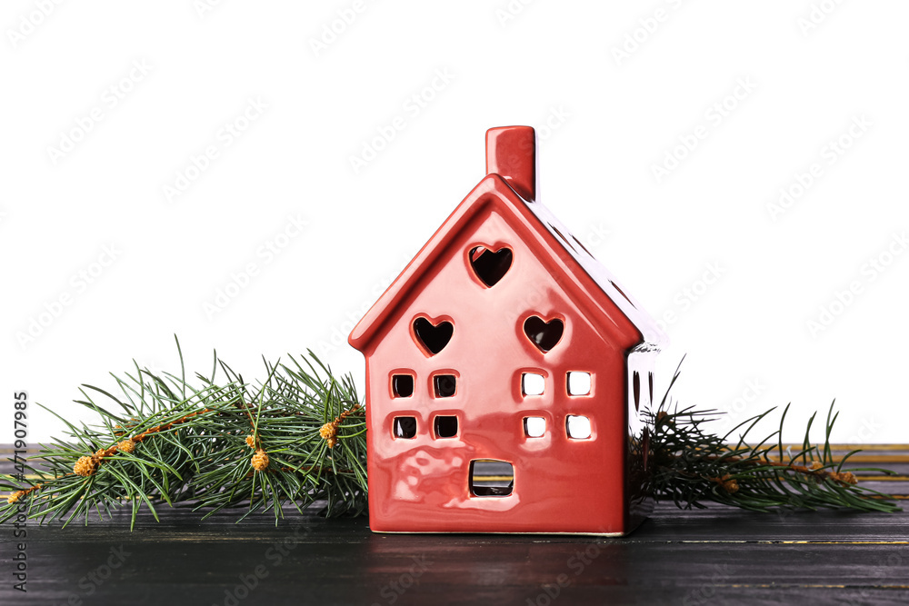 Toy house and fir branches on table against white background. Winter concept