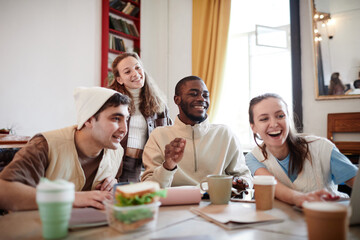 Group of friends laughing and looking something on laptop while sitting at the table in the room