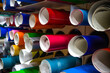 Round rolls of self-adhesive film in the production of interior advertising. Stand for the production of pasting vehicles. Multicolored vinyl film in tubes on the stand.
