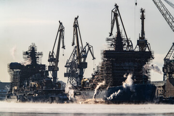  The construction of nuclear icebreakers, cranes of of the Baltic shipyard in a frosty winter day, steam over the Neva river, smooth surface of the river