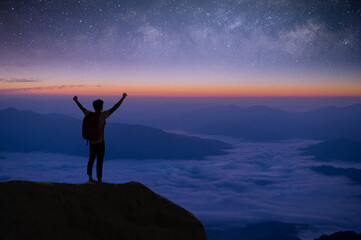 Wall Mural - Silhouette of young traveler and backpacker standing and open both arms watched the star and milky way alone on top of the mountain. He enjoyed traveling and was successful when he reached the summit.