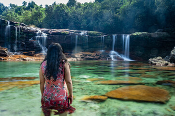 girl standing with waterfall flowing streams and calm blurred clear water at morning long exposure