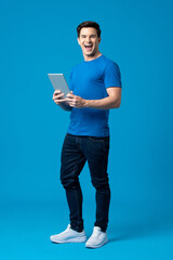 Surprise young handsome Caucasian man smiling and holding laptop computer in isolated light blue studio background