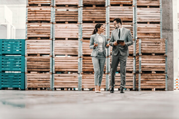 Business talk and walk in the warehouse. Man and a woman in a business suit stand in a warehouse and check the situation. Man holds a tablet in his hand and points a finger at the woman at something