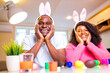 © yurakrasil - Young african american man and woman wearing cute easter bunny ears and painting eggs in the house