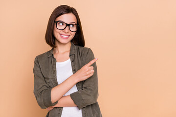 Wall Mural - Photo of cheerful lady indicate forefinger empty space banner wear specs khaki shirt isolated beige color background