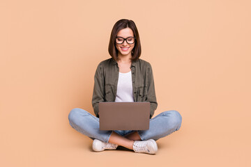 Wall Mural - photo of cheerful positive programmer lady sit floor hold pc wear eyewear khaki shirt isolated beige