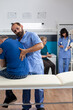 Osteopathic nurse stretching spinal cord and shoulder of aged patient with injury for physiotherapy. Chiropractor giving assistance to senior man with back pain for physical recovery