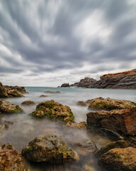 There are several rocks in the foreground with silky water, a horizon bordered by a murky, moving sky. Cabo de Palos(Murcia-Spain)