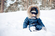 © Lyubov - Portrait of child sitting in snow in spruce forest. Little kid boy having fun outdoors in winter nature. Christmas holiday. Cute toddler boy in blue overalls and knitted scarf and cap walking in park.
