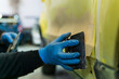 Close up view of an Auto mechanic repairing a yellow car with putty for paint in a workshop
