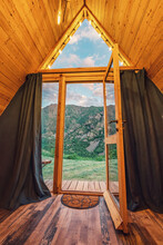 View From A Small Wooden Chalet House In The Mountains Outside Through A Glass Door And Window. The Concept Of Glamping And Idyllic Holidays