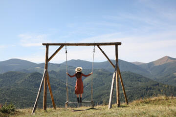 Wall Mural - Young woman on outdoor swing in mountains, back view