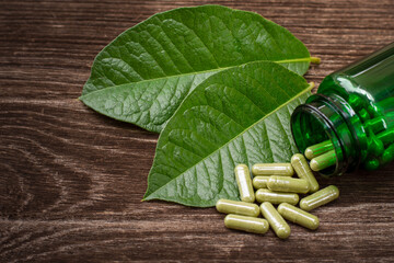 Canvas Print - Kratom leaf (Mitragyna speciosa) with kratom powder capsules in glass bottle isolated on wooden table background. 