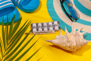 Wall Mural - Top view on white pills in blister pack, thermometer, blue hat, blue flip-flops, sunglasses, seashell, palm leaf on yellow background. Concept of beach holiday, sea tour, warm sunny summer